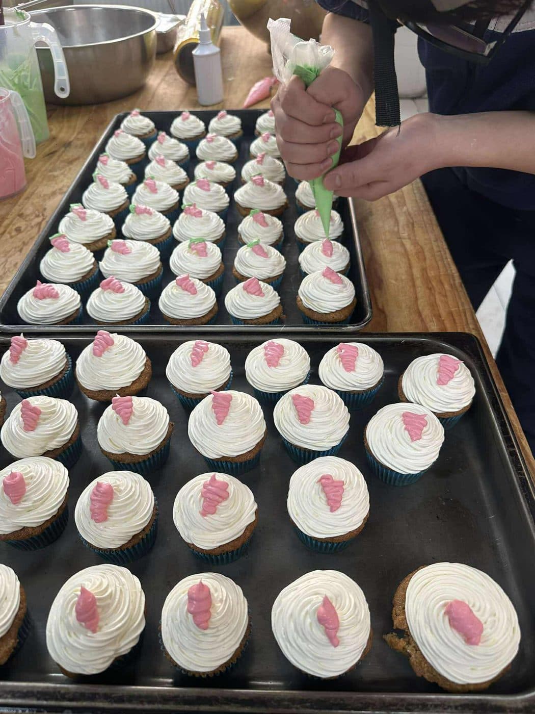 A cook piping cream onto cupcakes